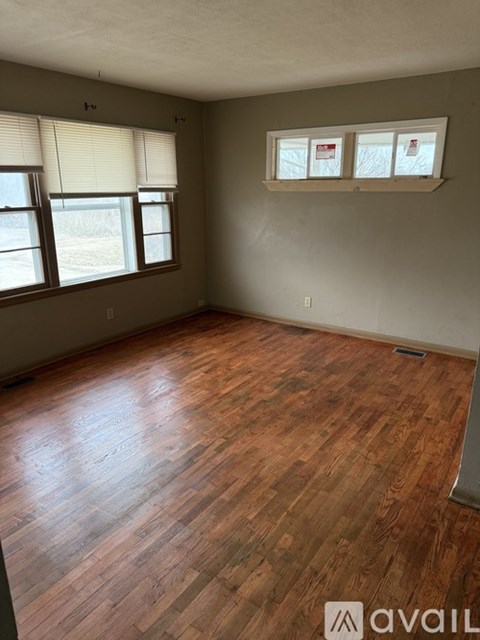 A room with wooden flooring and two windows.