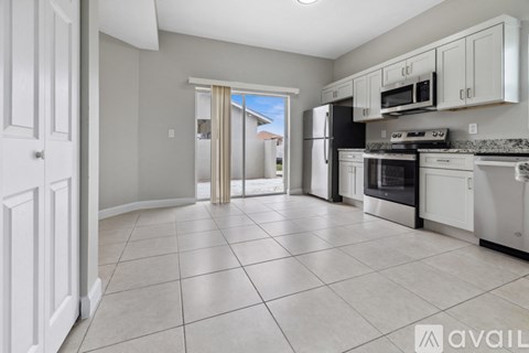 A kitchen with white cabinets and appliances, a tiled floor, and a doorway leading to a balcony.