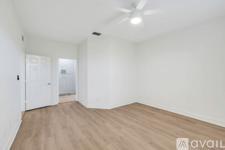 A room with wooden flooring and white walls, with a ceiling fan and a door.