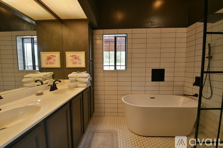 A bathroom with a white tub, two sinks and a window.
