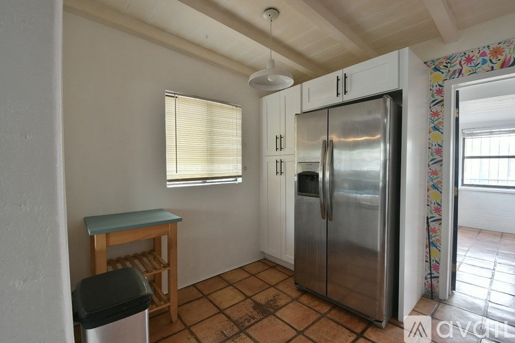 A kitchen with a refrigerator, table, and trash can.