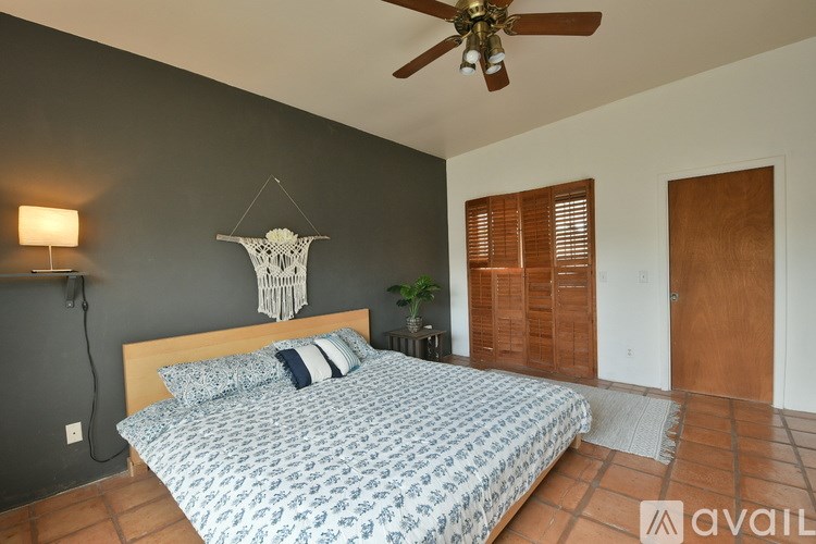 A bedroom with a bed, a ceiling fan, and a wall hanging.