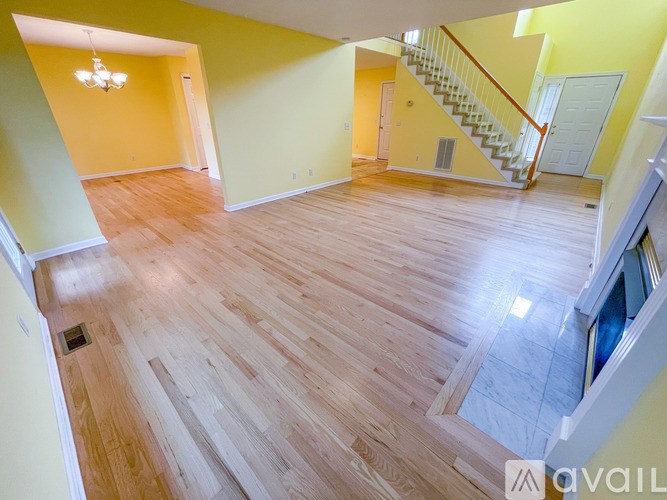 A spacious room with wooden flooring and a staircase.