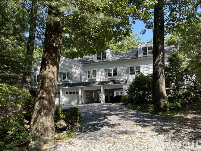 A large white house with a grey roof is surrounded by trees.