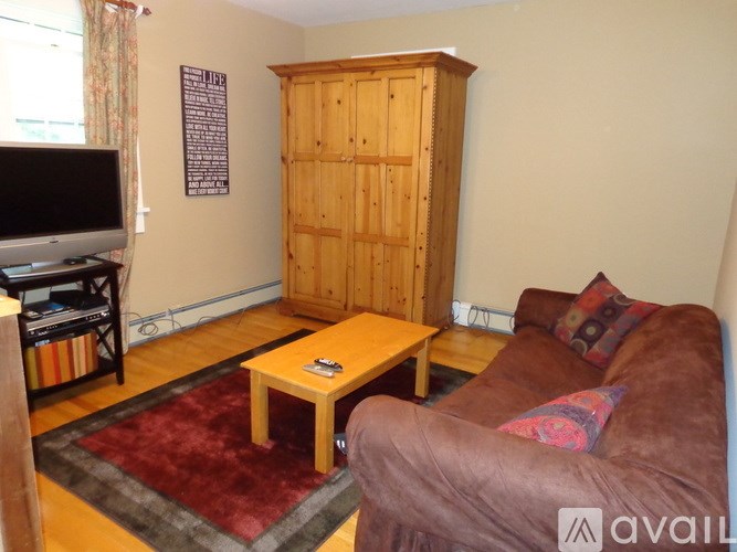 A living room with a brown couch, a wooden cabinet, and a TV.