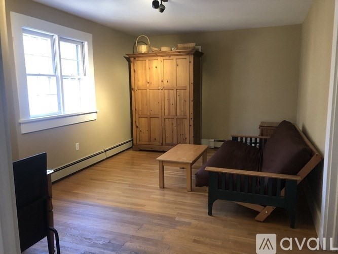 A room with a wooden floor, a wooden cabinet, a brown sofa, and a small table.