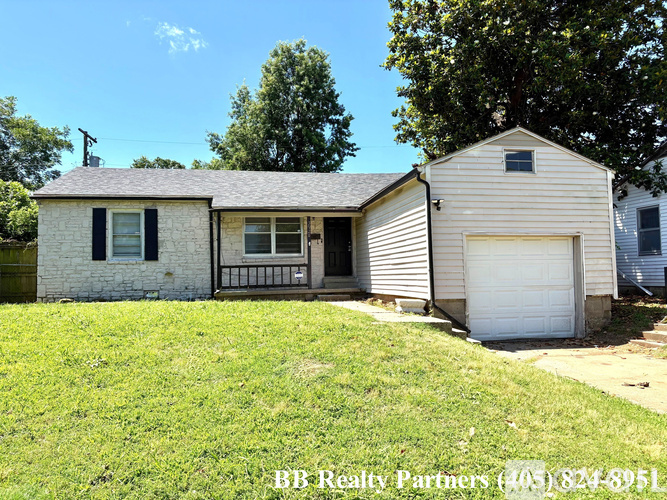 A white house with a black window and a garage door is for sale.