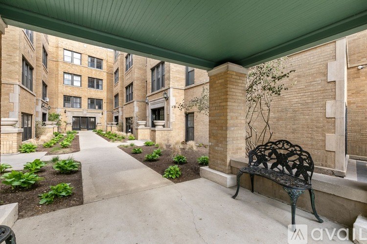 A black metal bench sits under a green awning on a concrete walkway.