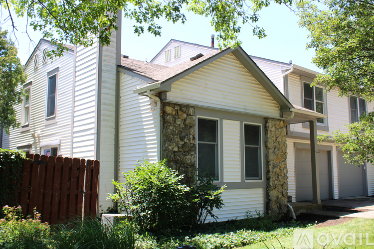 A house with a white siding and a stone pillar in front of it.