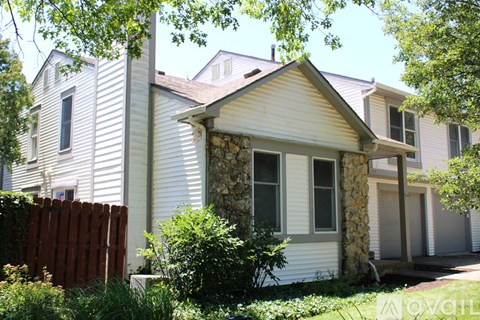A house with a white siding and a stone pillar in front of it.
