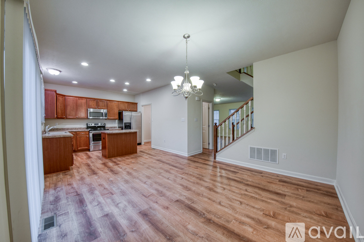 A large, empty living room with wood flooring and a staircase in the background.