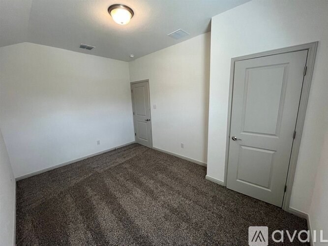 A carpeted room with a door and a wall-mounted light fixture.