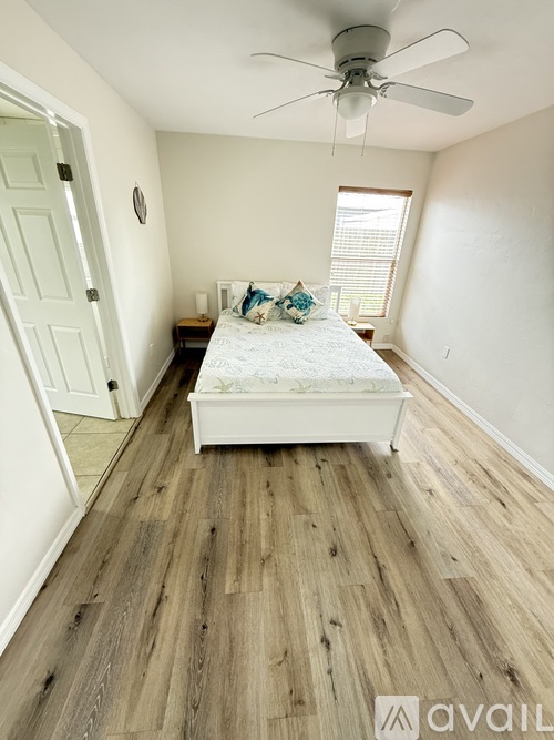 A bedroom with a bed, wooden floor, and a ceiling fan.
