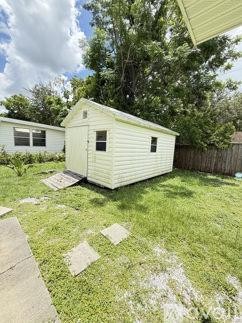 A small white shed sits in a grassy backyard.