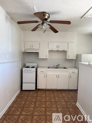 A kitchen with white cabinets and a brown ceiling fan.
