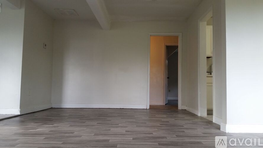 A room with a wooden floor and white walls, with a doorway leading to another room.