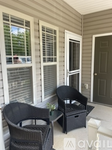 Two black chairs are on a porch with a table between them.