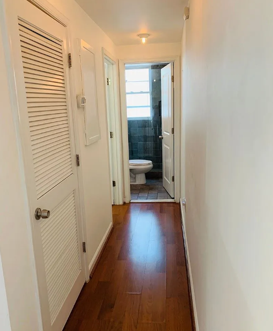 A hallway with a toilet visible through the door.