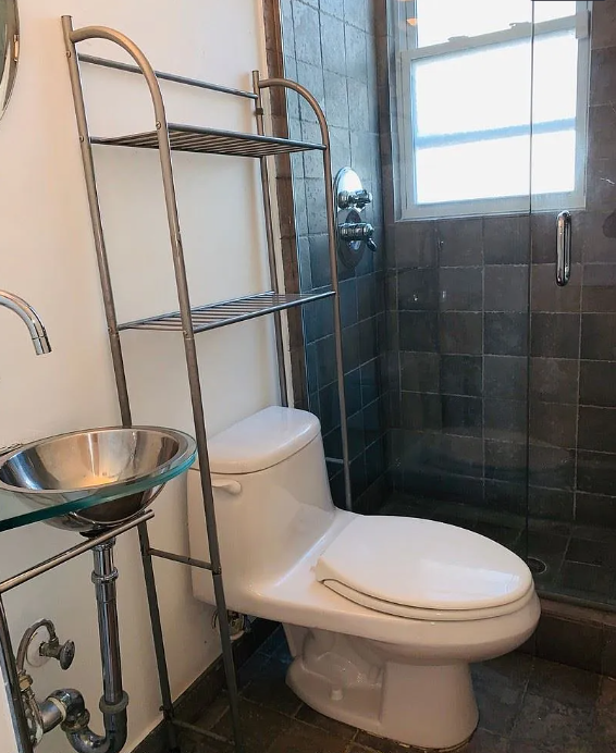 A white toilet sits next to a metal shelf in a bathroom.