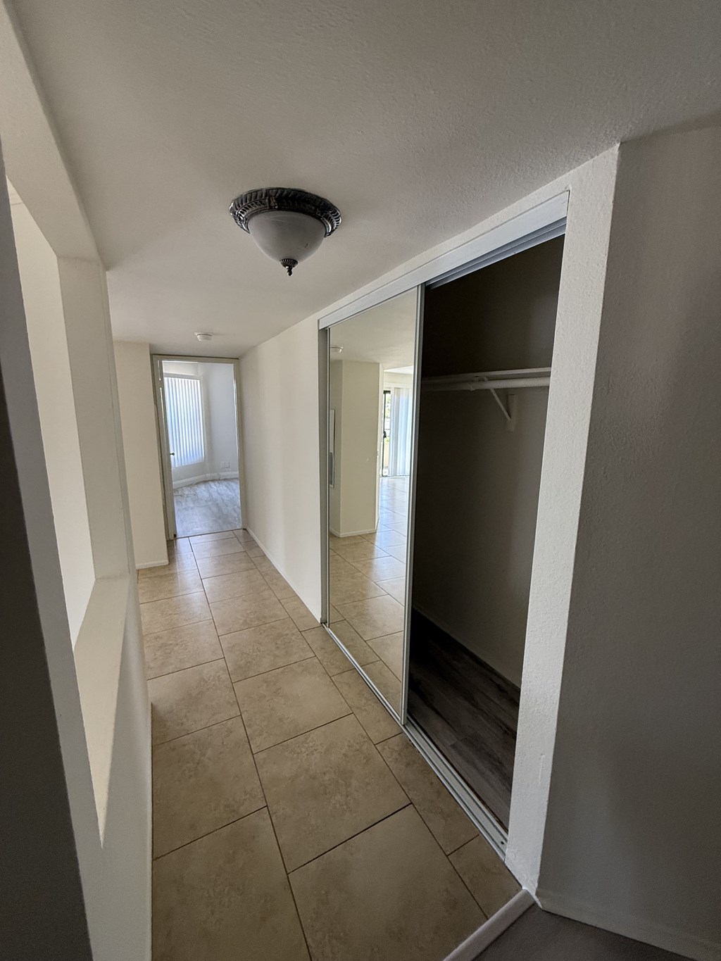 A hallway with a tiled floor and a mirror on the wall.