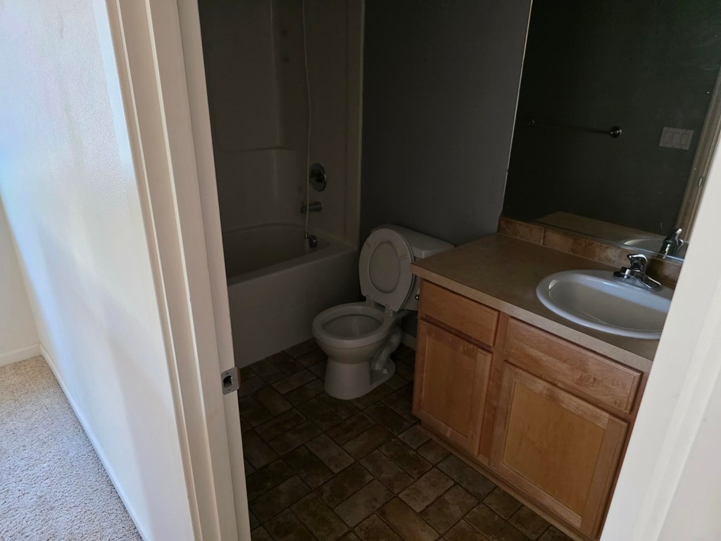 A bathroom with a toilet, sink, and wooden cabinets.