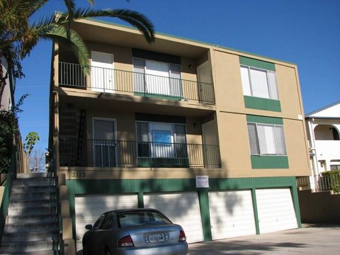 A car is parked in front of a building with a balcony.