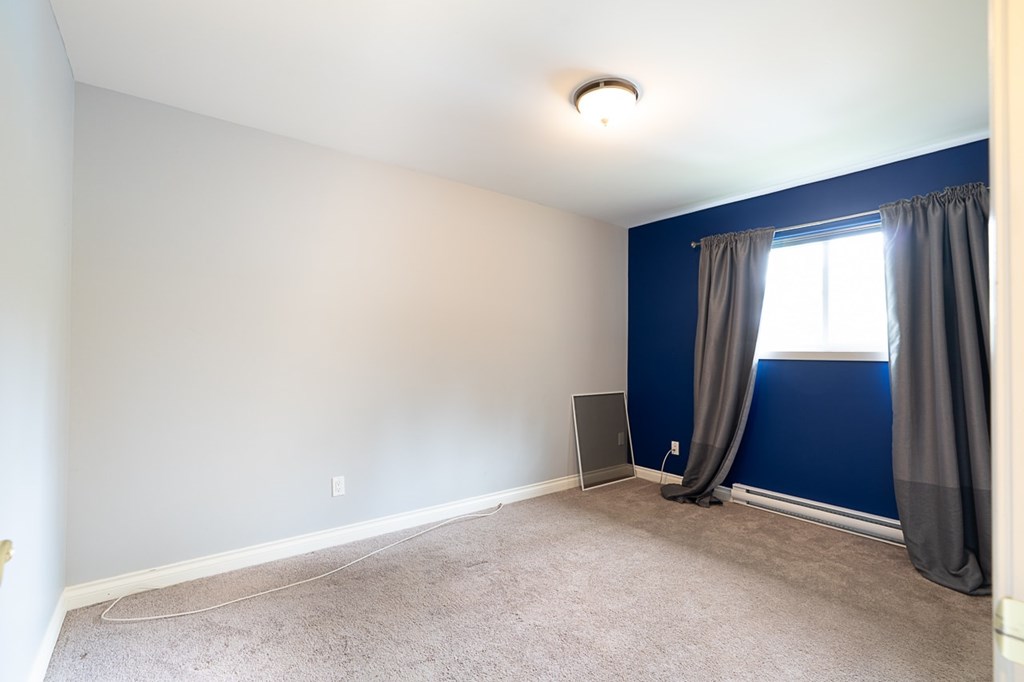 A room with a carpeted floor and a window with curtains.