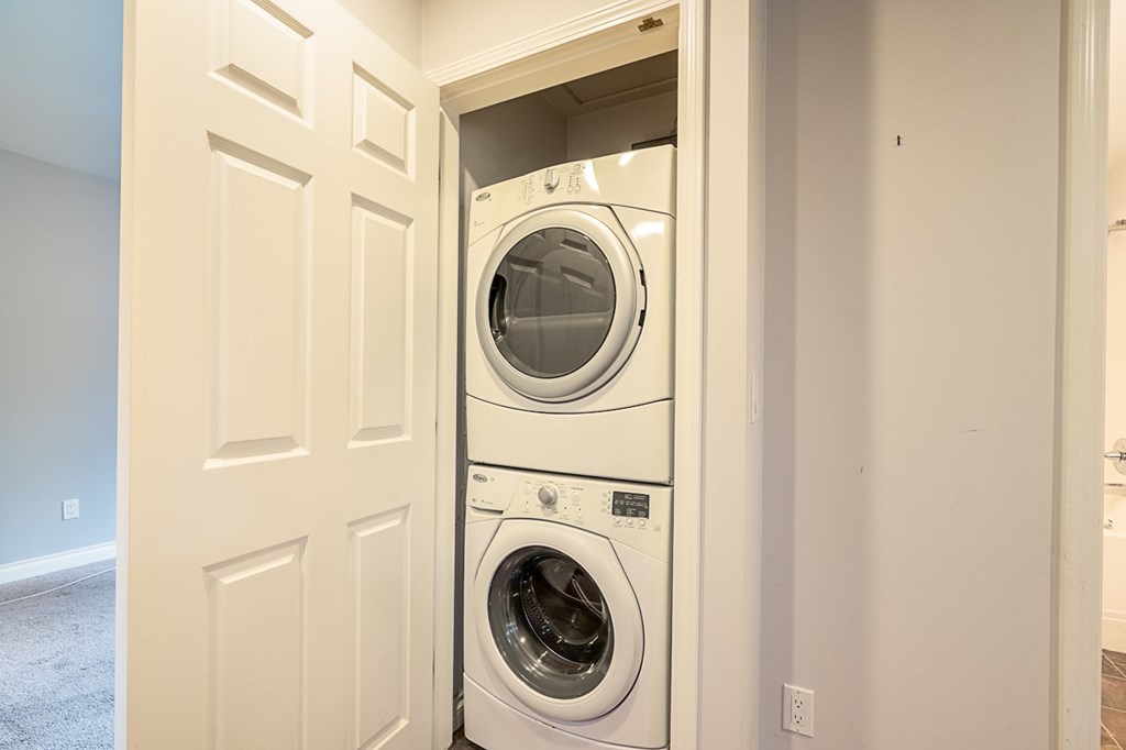 A white door is open to reveal a stacked washer and dryer.