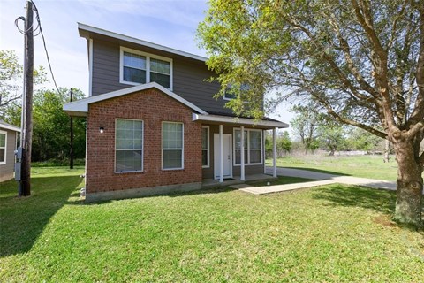 A house with a grey roof and a brick facade is surrounded by a grassy lawn.