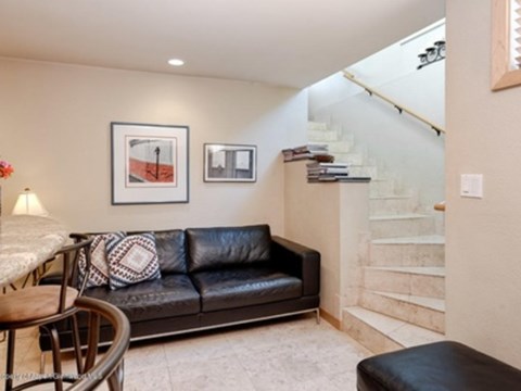 A living room with a black leather couch and a staircase in the background.