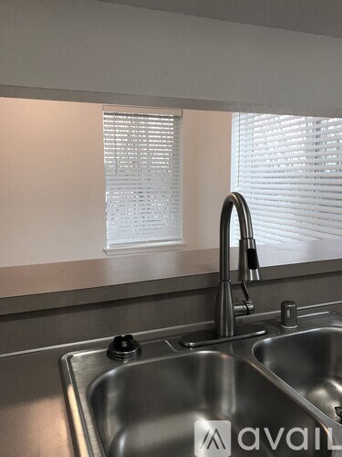 A kitchen sink with a faucet and a window with blinds behind it.