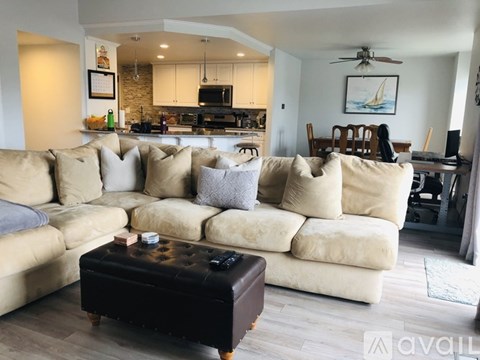 A living room with a beige couch and a black ottoman.