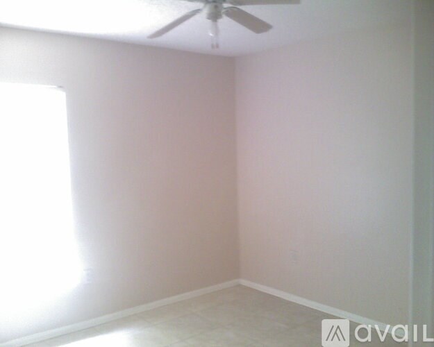 A room with a ceiling fan and a window letting in sunlight.