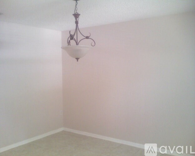 A chandelier hangs from the ceiling in a room with white walls and carpeted floor.