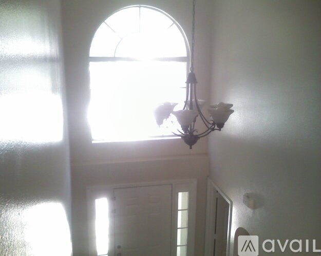 A chandelier hangs in a room with a large arched window.