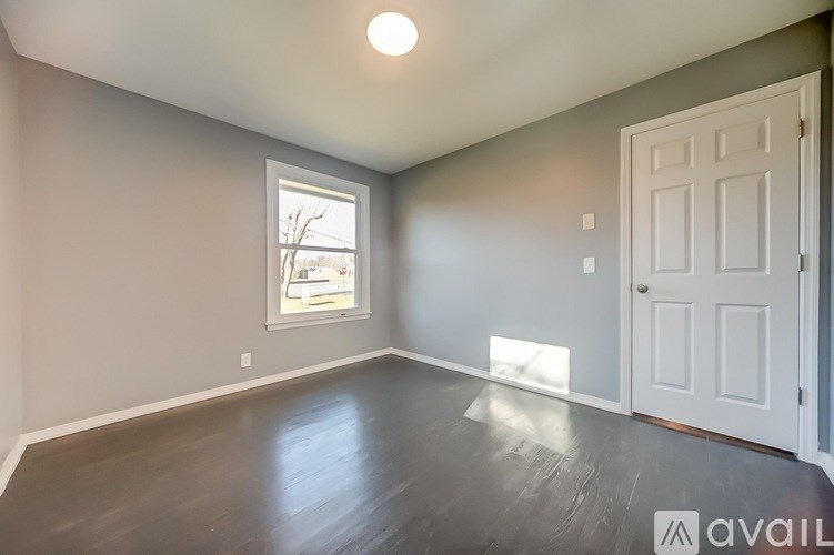 A room with a white door and a window with a view of trees and a house.