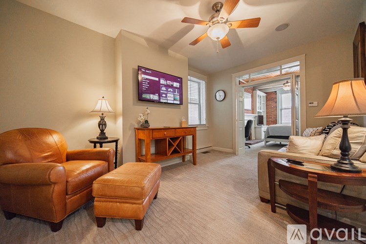 A living room with a brown leather chair, a brown ottoman, a wooden coffee table, and a flat screen TV mounted on the wall.