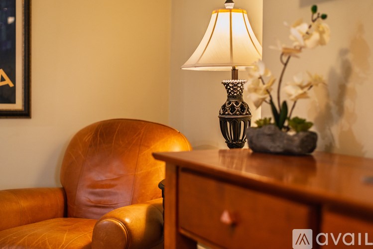 A brown leather chair sits next to a table with a lamp and flowers on it.
