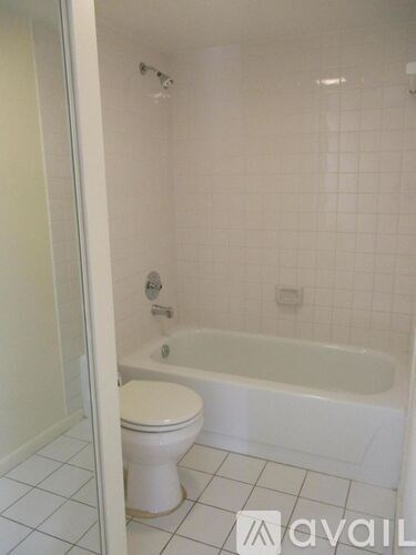 A white toilet is in a white tiled bathroom with a white bathtub.