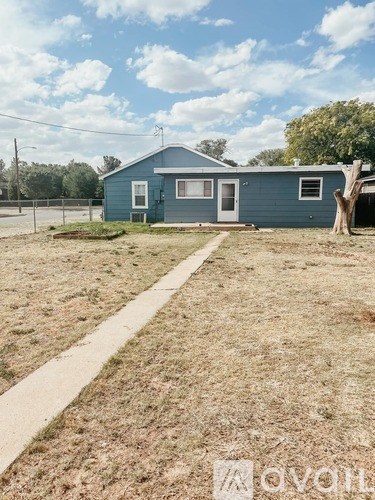 A blue house with a white door and windows is surrounded by a grassy area.