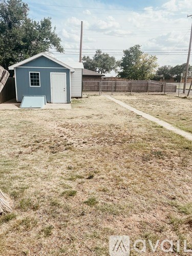 A small blue shed sits in a grassy field with a fence in the background.