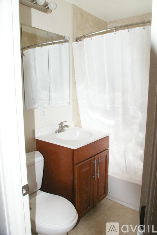 A white toilet is in a small bathroom with a wooden cabinet and a sink.