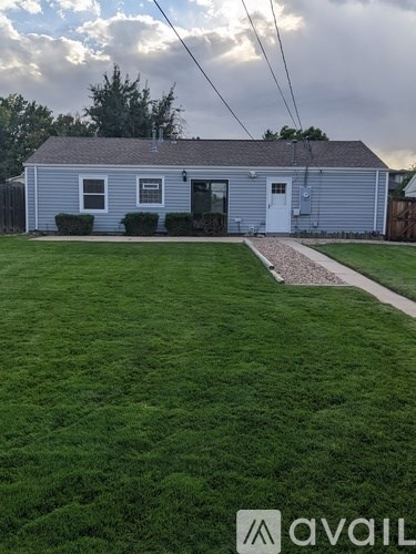 A house with a grey roof and a white door is surrounded by a grassy lawn.
