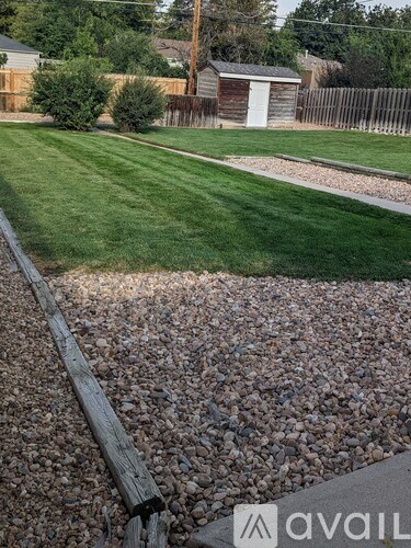 A gravel area in the foreground with a wooden fence and a house in the background.