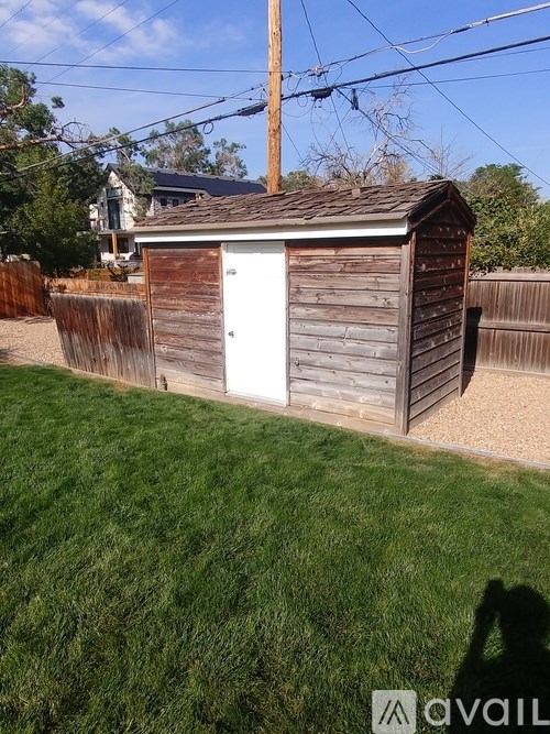 A small wooden shed with a white door is situated in a grassy area.