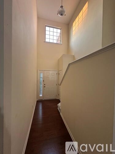 A hallway with a wooden floor and white walls leading to a door.