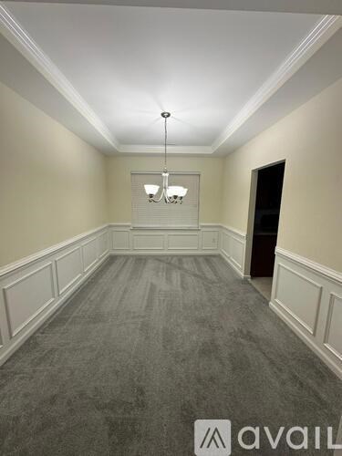 A large empty room with a carpeted floor and a chandelier hanging from the ceiling.
