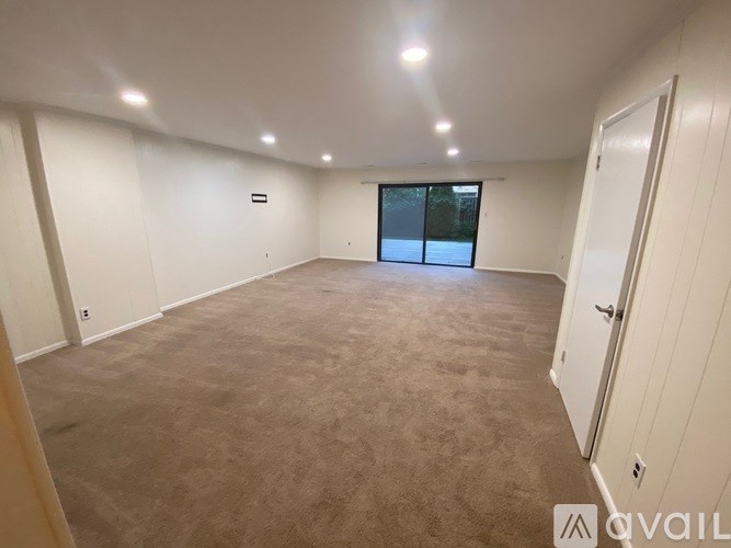 A spacious room with beige carpeting and white walls is available for rent.