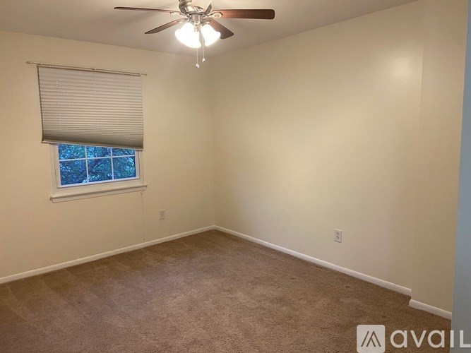 A room with a carpeted floor, a ceiling fan, and a window with blinds.