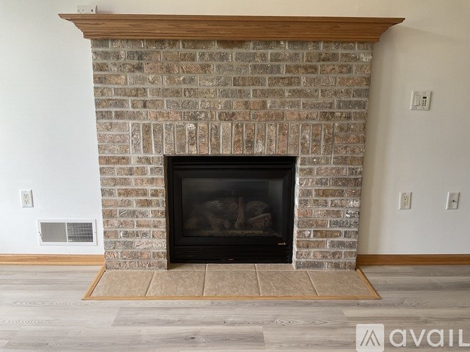 A brick fireplace with a wood mantle and a fire burning inside.